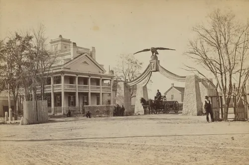Black-and-white photo of the ornate Beehive House. Two people stand in the street in the foreground.