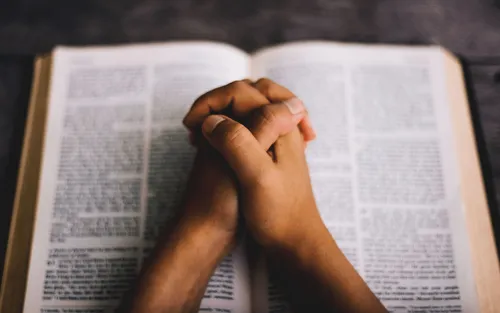 hands folded in prayer, resting on an open Bible
