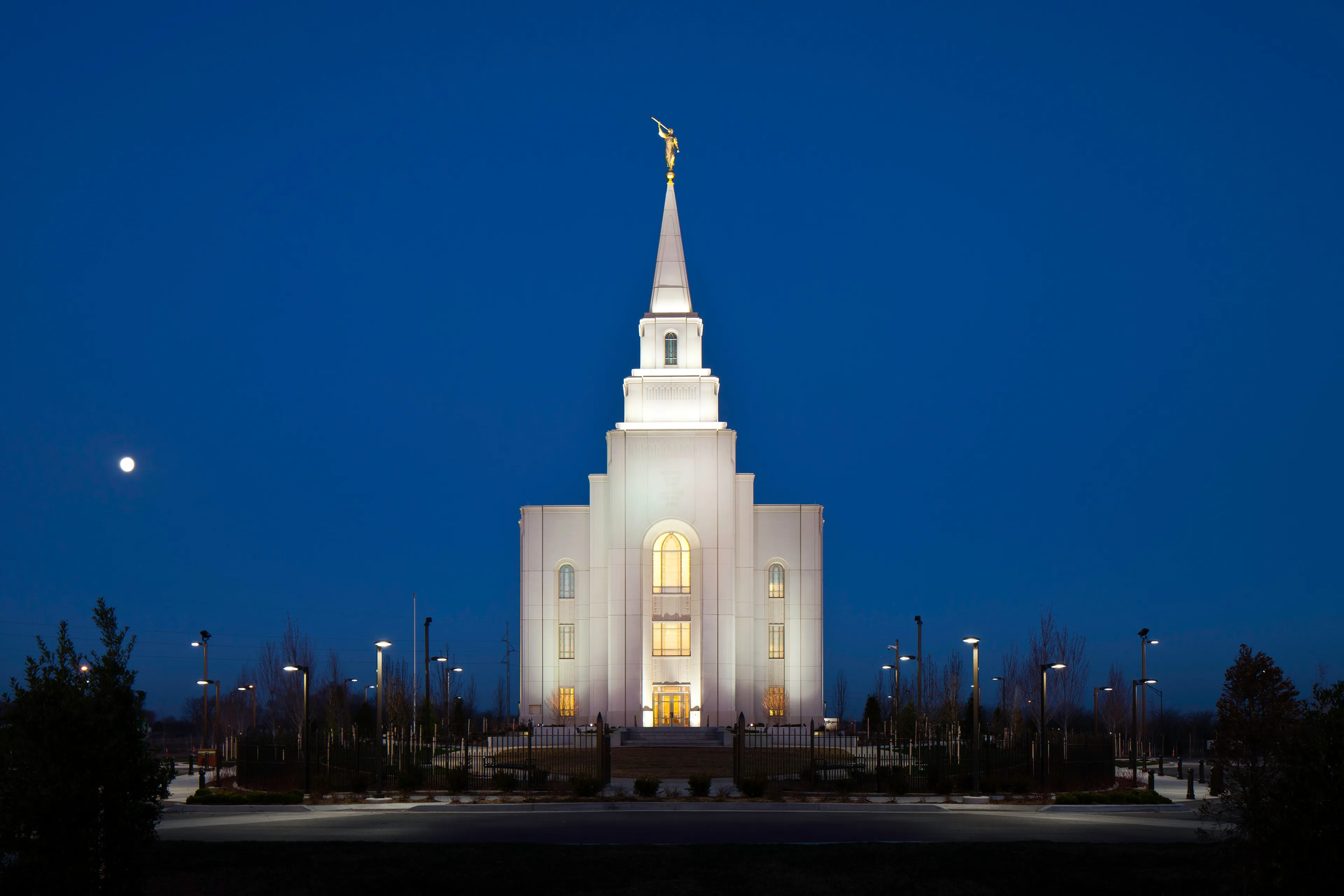 The Kansas City Missouri Temple lit up in the evening, including scenery.  