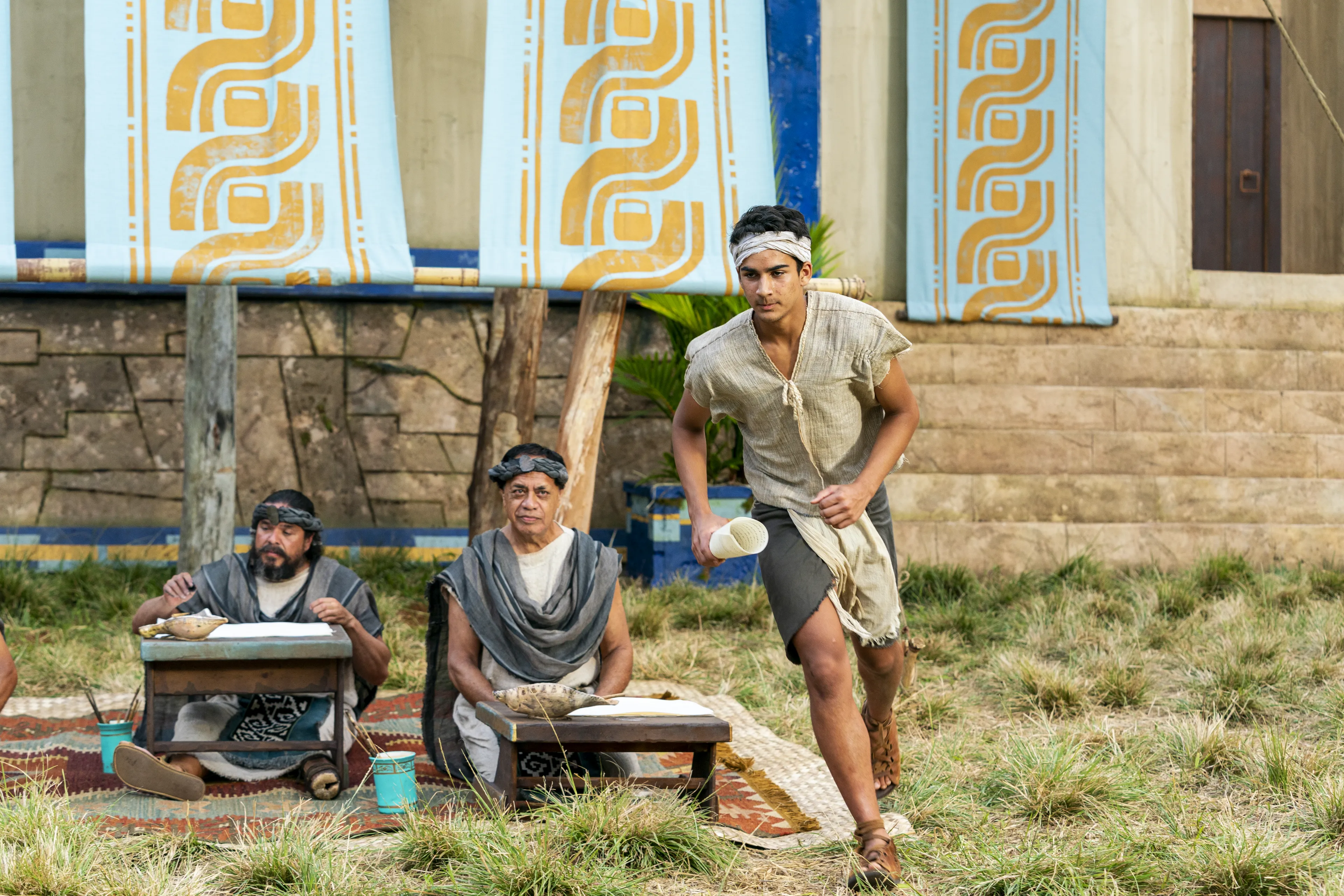 Scribes sit, taking notes of what King Benjamin is teaching. Runners take the parchment to the Nephite people in the Land of Zarahemla.