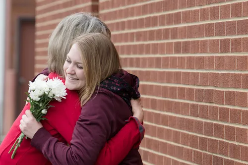A young adult and a woman share a hug and flowers. 