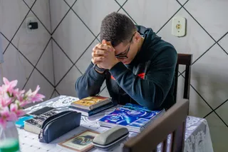 A young man folds his arms and prays in his home in Brazil. 