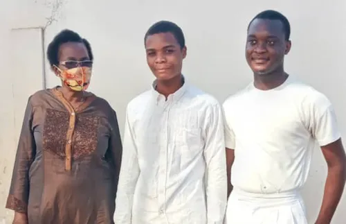 two young men in baptismal clothes with a woman wearing a mask