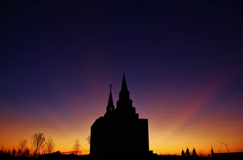A silhouetted image of the Kansas City Missouri Temple, with the orange and purple colors of the sunset in the background.