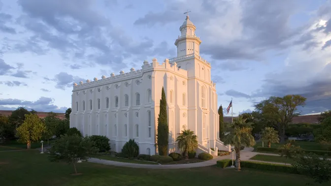 Early morning photograph of the St. George Utah Temple with the sun illuminating the East side of the Temple. Morning clouds whisk through the sky.