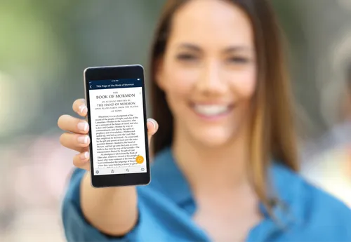young woman holding mobile phone with Book of Mormon on screen