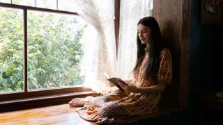 A young woman reading the scriptures by an open window