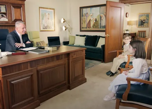 Elder Soares sitting at his desk and talking to children