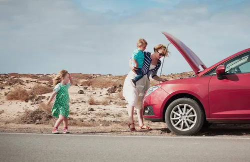 woman looking at broken-down car with children