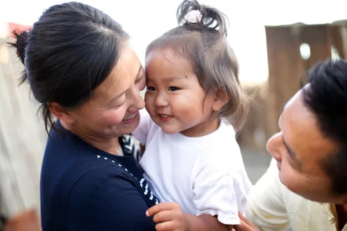 A mother holds her little girl in her arms and puts her nose against the little girl’s cheek.