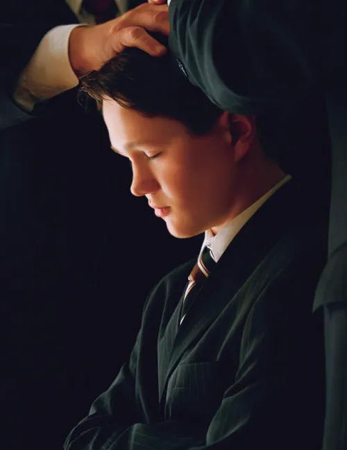 A photograph by Ruth Schonwald showing a young dark-haired man in a black suit being ordained to the priesthood by several men.