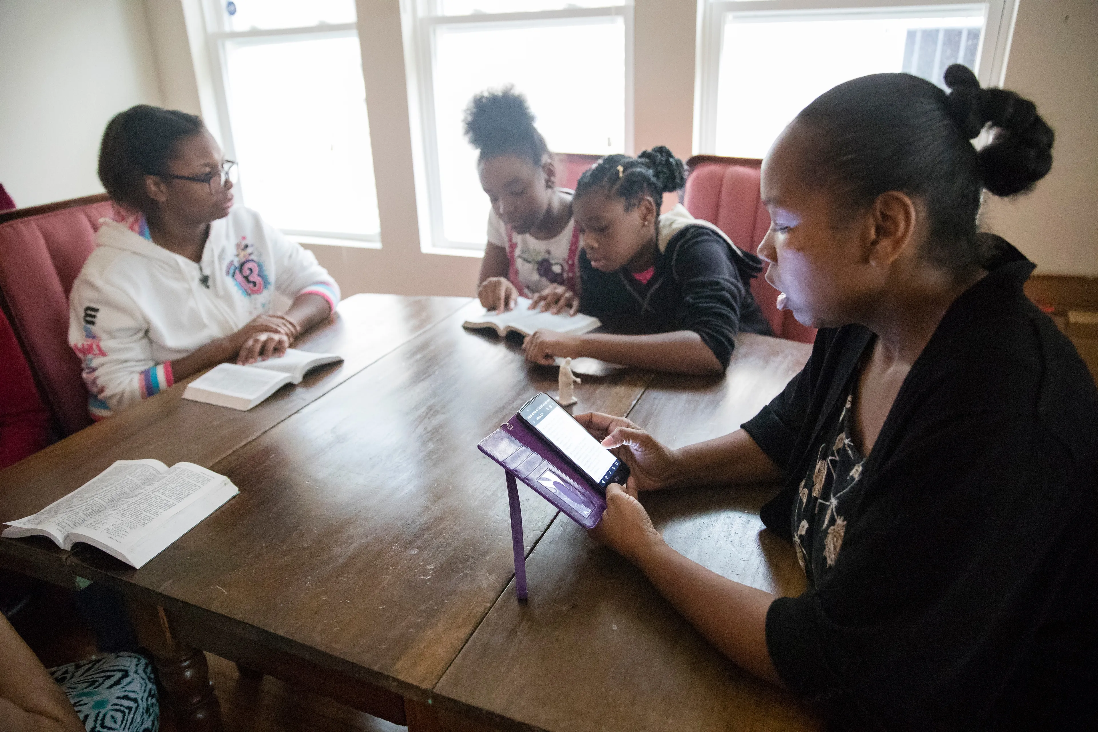 Family members sit down together to read the scriptures from books and smartphones.