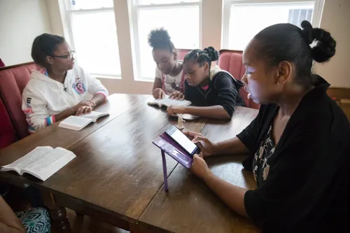 Family members sit down together to read the scriptures from books and smartphones.