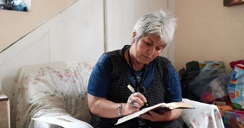 Woman writes in a book while seated in a chair.