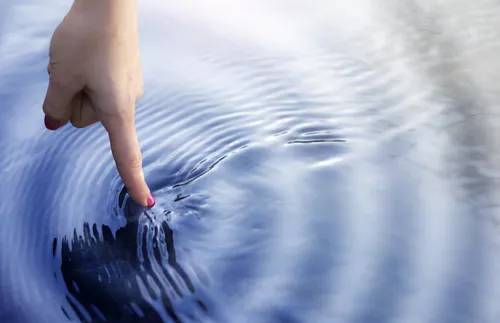 finger touching water and making ripples