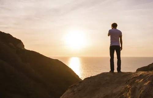 young adult man standing atop a mountain