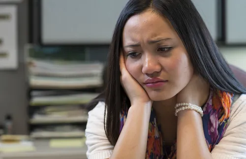 Asian woman sitting at a desk looking very sad and emotional.  She looks like she is ready to cry.