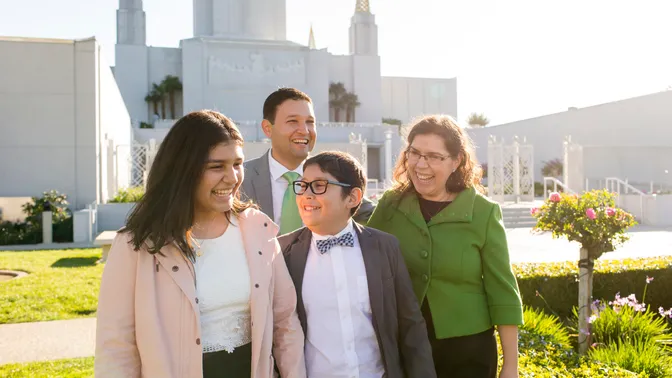 A father and mother  talk and interact with their children as the walk around the grounds in front of the Oakland Temple.