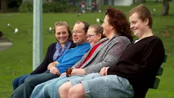 A family of five sitting on a park bench together