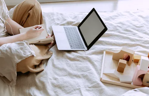 Woman taking notes on bed with laptop