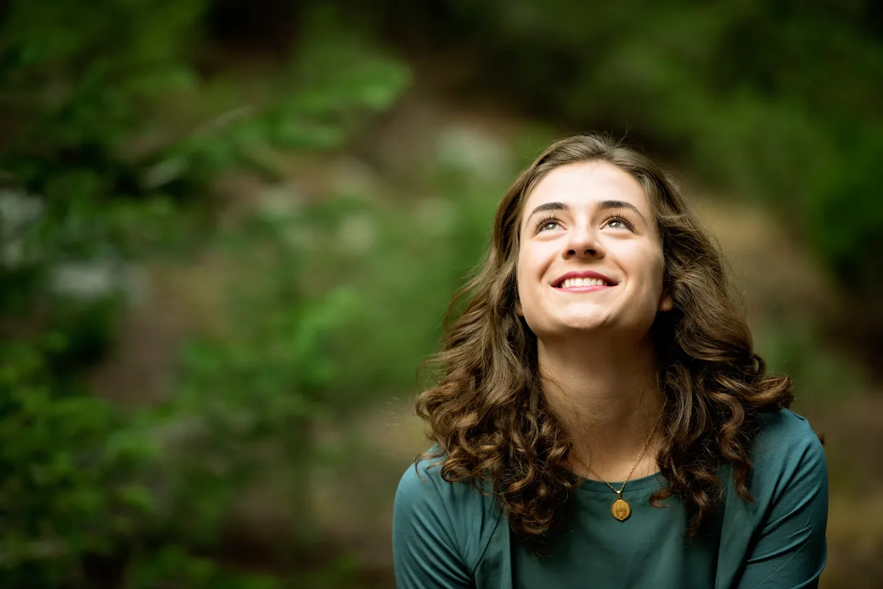 A woman smiles in a field contemplating the love of God, and Jesus Christ found in the Bible