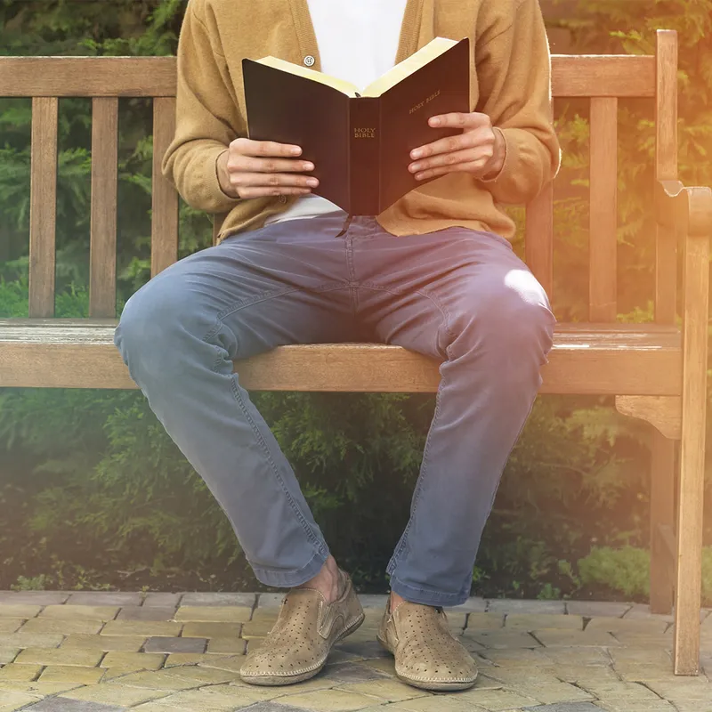 A man studies the scriptures on a park bench learning that baptism for babies is not necessary