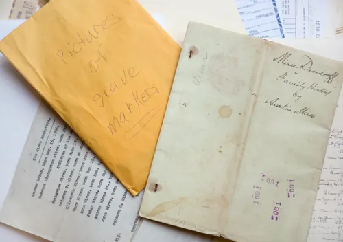 Pile of family history documents -- family histories, envelopes, grave markers, letters, certificates, papers, etc.