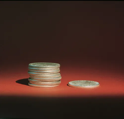 A stack of nine silver coins next to a single silver coin on a red background, with a single light source casting shadows.
