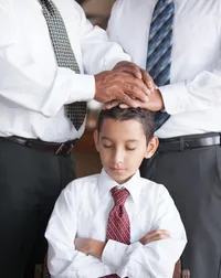 A young boy in a white shirt and tie being confirmed by two men.