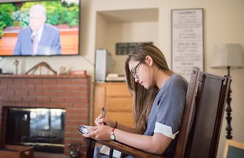 young woman taking notes during general conference