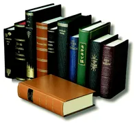 An English language reproduction copy of the original 1830 edition of the Book of Mormon is lying on a desk.  Several non-English language copies of the Book of Mormon are standing upright behind it.