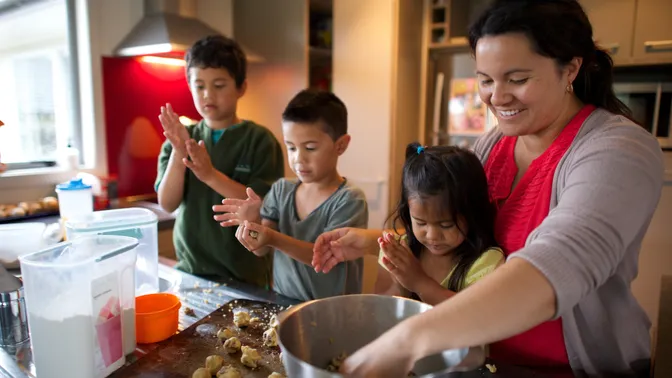 A mother bakes cookies with her three children in the kitchen.