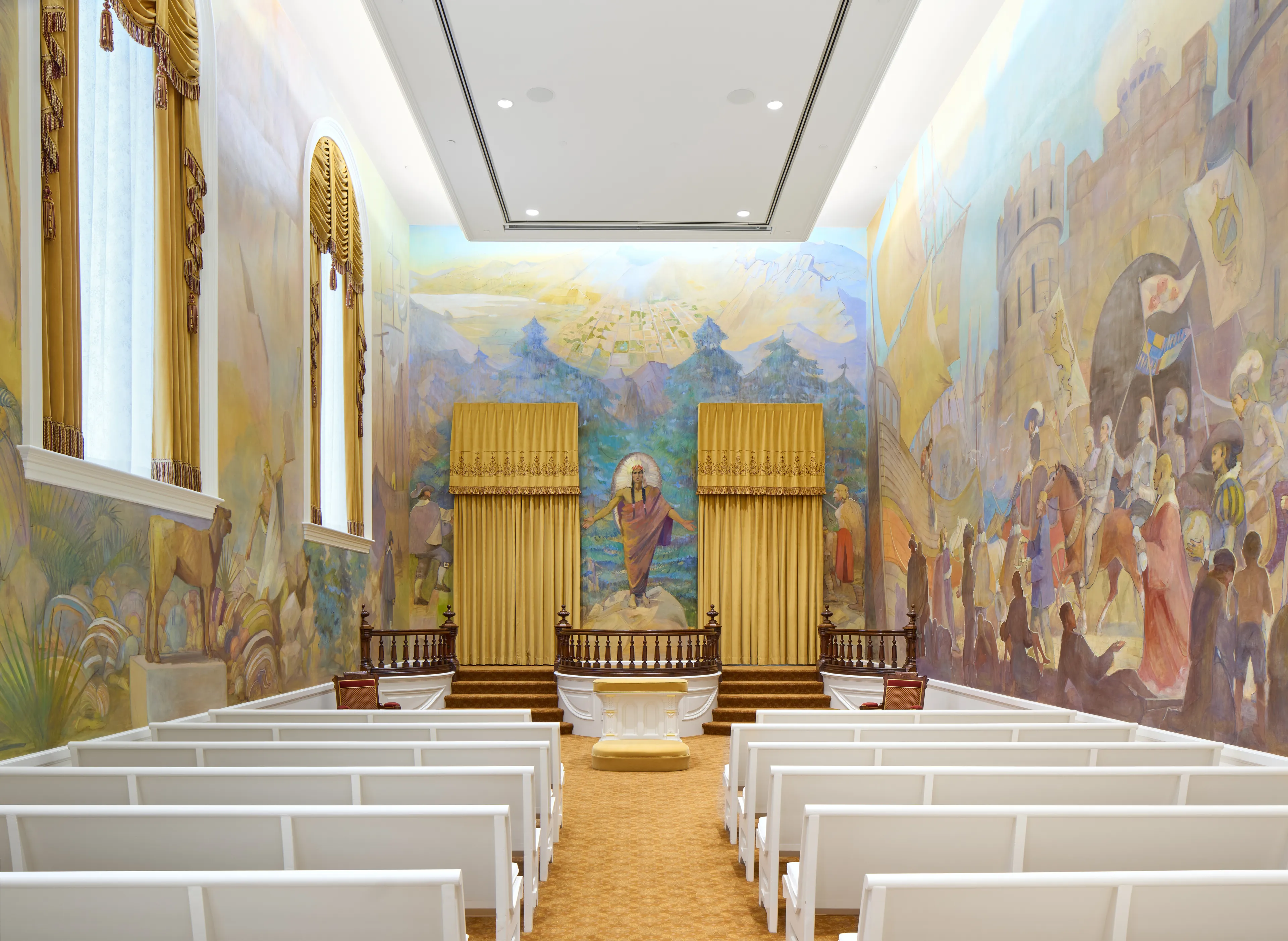 Interior image of the Manti Utah Temple. The image focuses on the Ordinance room. You see pews in the room. Around the walls are murals.