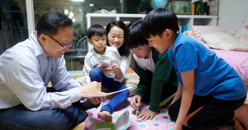 Family playing games on the floor and studying scriptures with happy smiles.