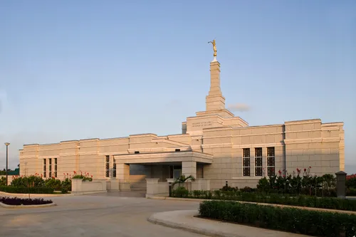 The front of the Aba Nigeria Temple on a clear, sunny day, with flowers growing near the entrance.
