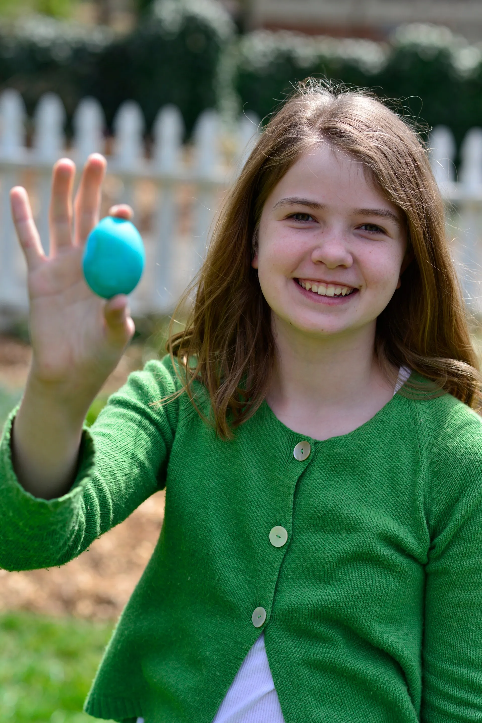 Niña que sostiene un huevo de Pascua azul al aire libre.