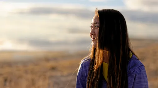 A young woman is outdoors and smiling. She is looking towards the camera. She is at Antelope Island State Park in Utah.