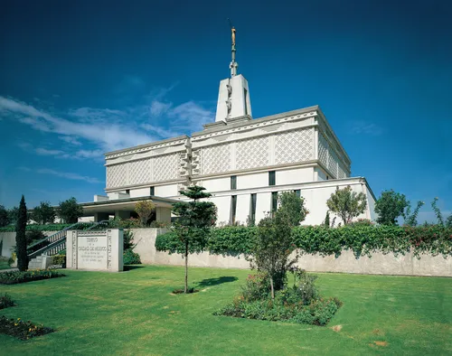 The Mexico City Mexico Temple viewed from the front entrance, with the name sign and trees and flowers in the daytime.