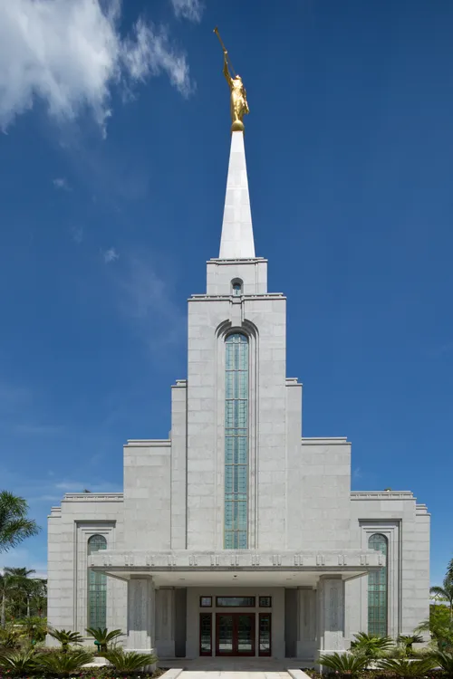 The front entrance of the Manaus Brazil Temple on a sunny day, with blue skies and light clouds behind.