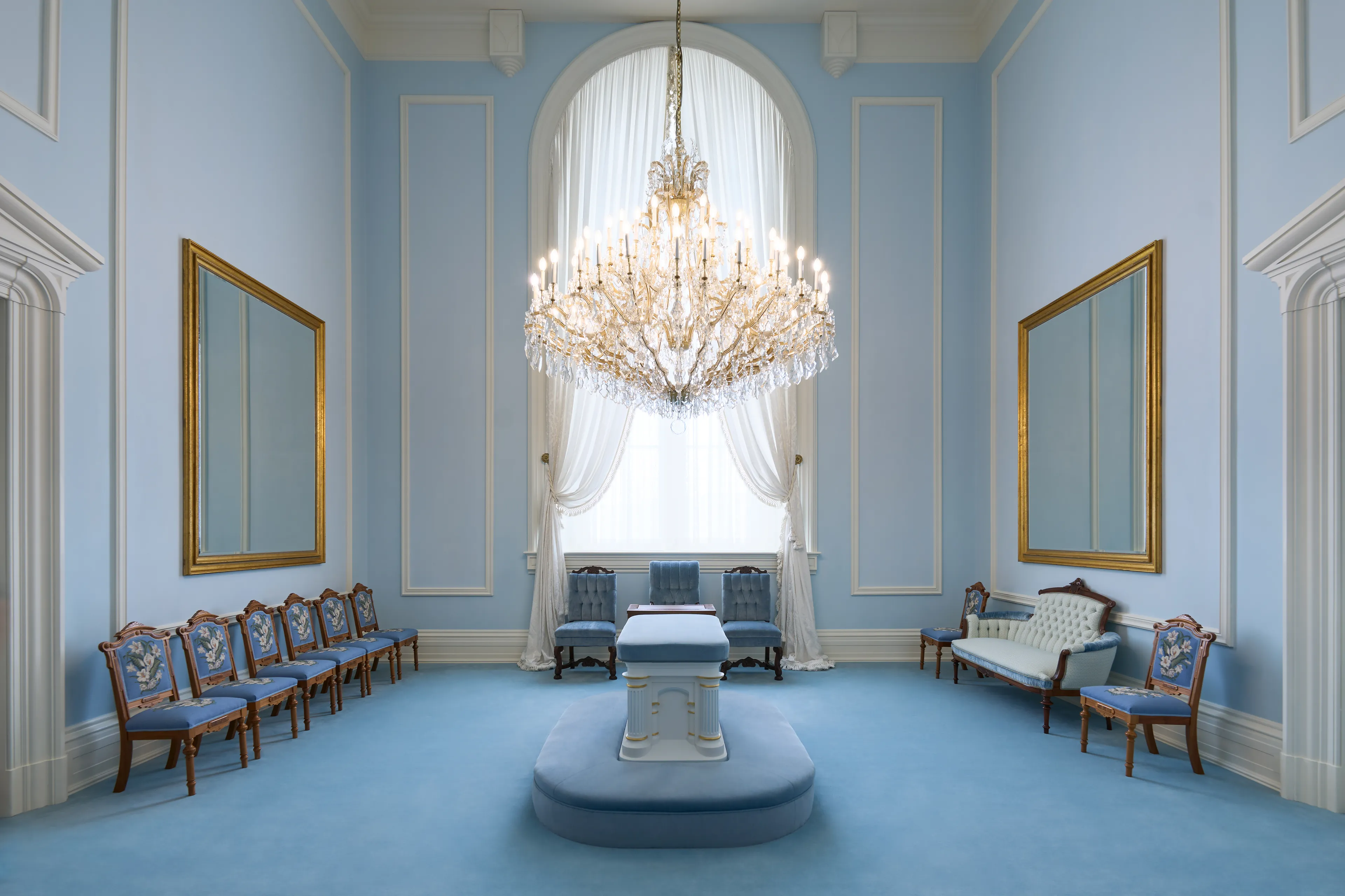 Interior image of the Manti Utah Temple. The image features a Sealing Room. There are chairs to two sides, an altar, and a chandelier.