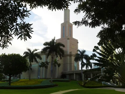 A side view of the Santo Domingo Dominican Republic Temple, with a partial view of the entrance and the grounds covered in trees.