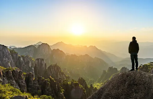 man standing on mountain and looking at sunset
