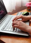 Hands are seen typing on a silver laptop with a computer mouse next to it.