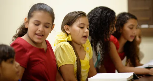 Young women of Hispanic descent in Sunday attire sing.