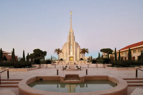 The exterior of the Rome Italy Temple at sunrise, with trees and a fountain.
