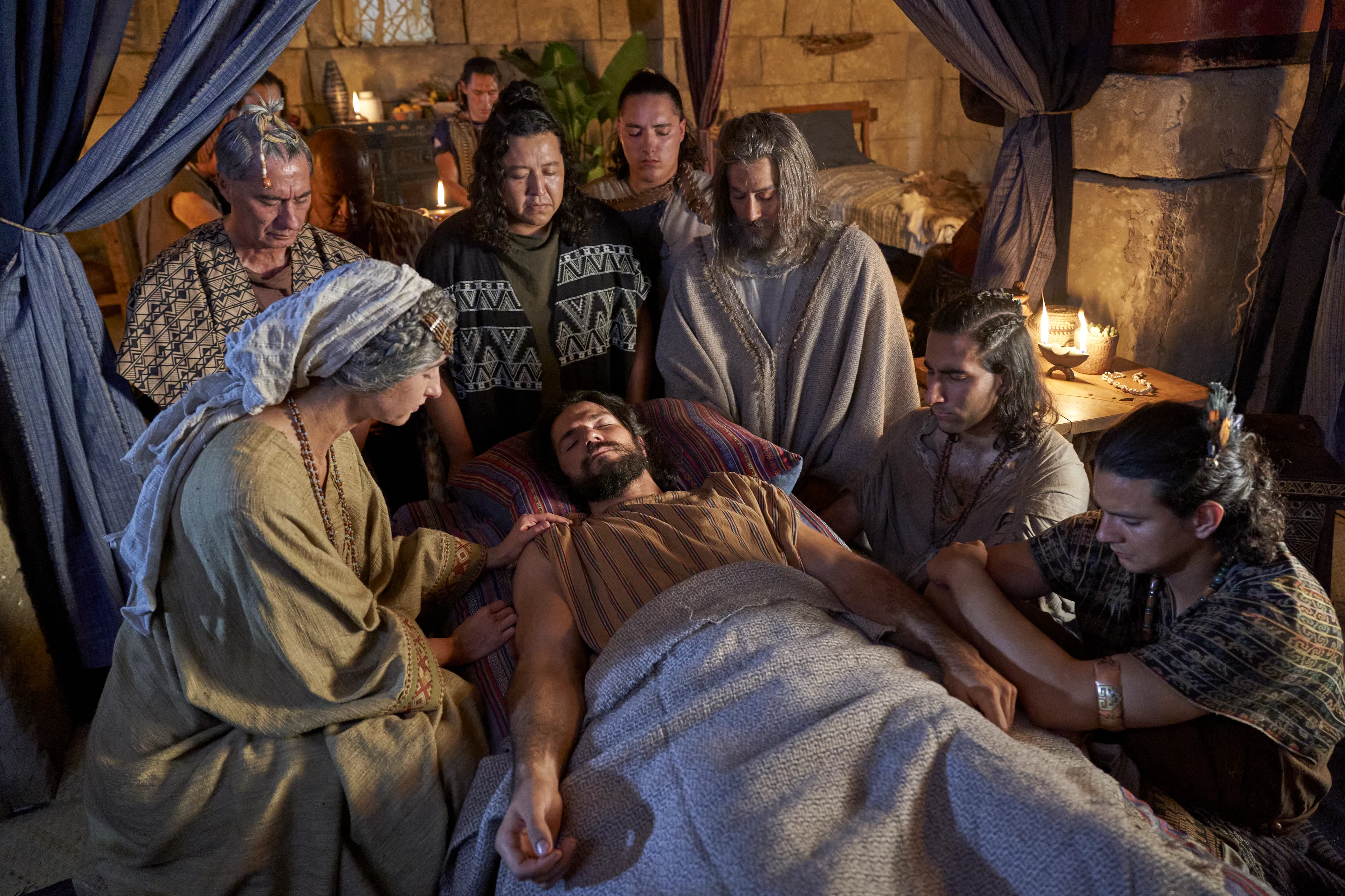 Alma the Younger lies on his bed struck dumb while family and priests kneel around him in prayer.