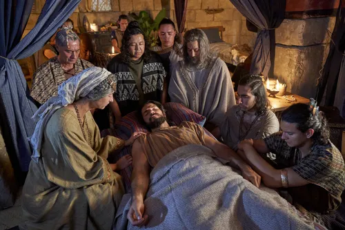 Alma the Younger lies on his bed struck dumb while family and priests kneel around him in prayer.