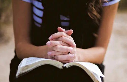 folded hands on top of open book
