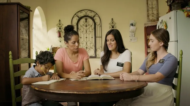 Two sister missionaries teach a woman about life after death studying from the Book of Mormon