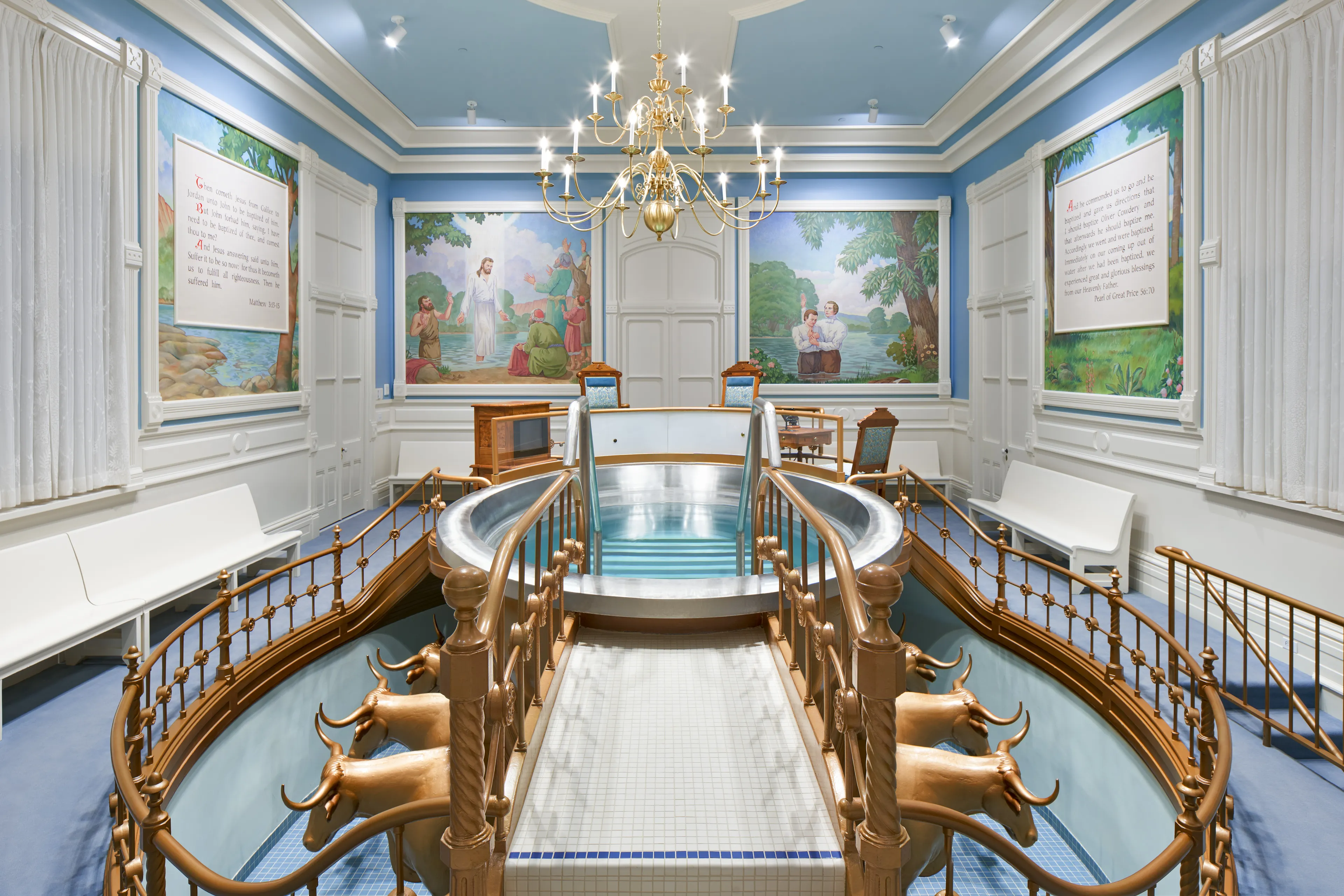 Interior image of the Manti Utah Temple. The image features the Baptistry. We see the font and the oxen below. There is art of the Savior painted on the walls around the font.